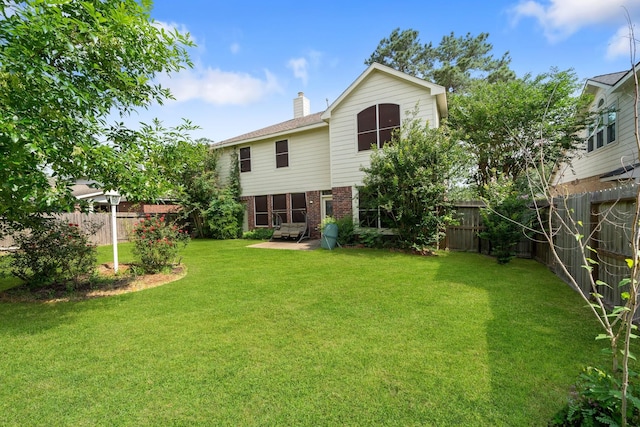 rear view of house featuring a lawn, brick siding, a chimney, and a fenced backyard