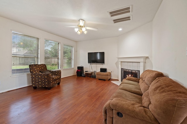 living room featuring visible vents, wood finished floors, baseboards, ceiling fan, and a tiled fireplace