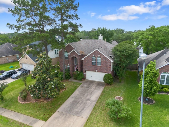 traditional-style home with a front lawn, a chimney, brick siding, concrete driveway, and an attached garage
