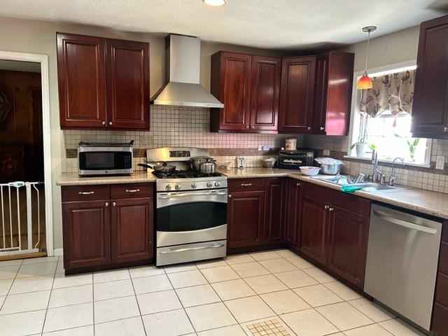 kitchen with a sink, stainless steel appliances, wall chimney range hood, light countertops, and dark brown cabinets