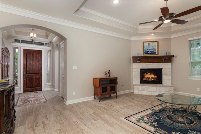 entryway featuring a stone fireplace, ceiling fan, a raised ceiling, arched walkways, and light wood finished floors