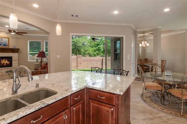 kitchen featuring visible vents, a tiled fireplace, a sink, ceiling fan with notable chandelier, and decorative light fixtures