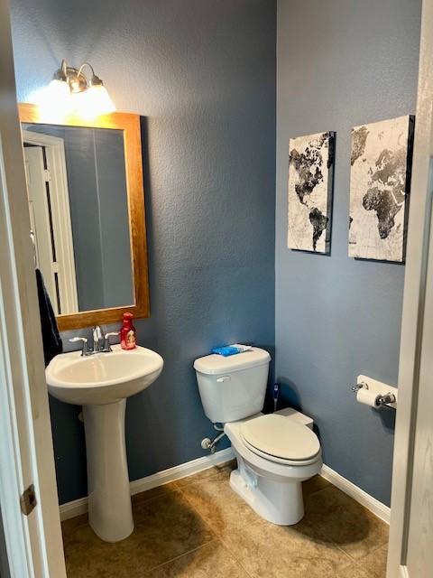 half bath featuring baseboards, a sink, tile patterned floors, and toilet