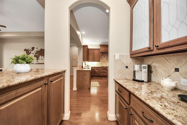 bar with a sink, light wood-type flooring, recessed lighting, arched walkways, and backsplash
