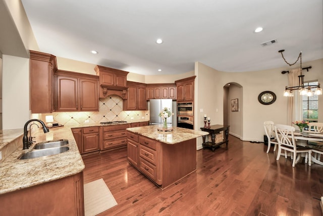 kitchen with visible vents, light stone countertops, arched walkways, a sink, and stainless steel appliances