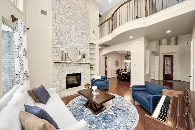 living room featuring visible vents, built in features, arched walkways, a fireplace, and a high ceiling