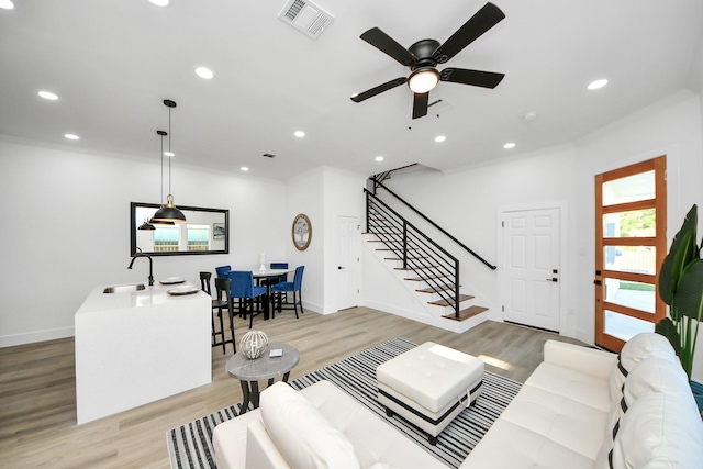 living area featuring stairway, light wood-type flooring, a ceiling fan, visible vents, and baseboards