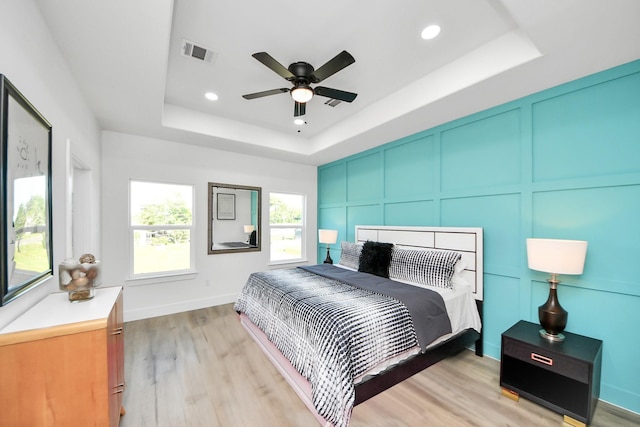 bedroom featuring visible vents, a decorative wall, a tray ceiling, and light wood-style floors