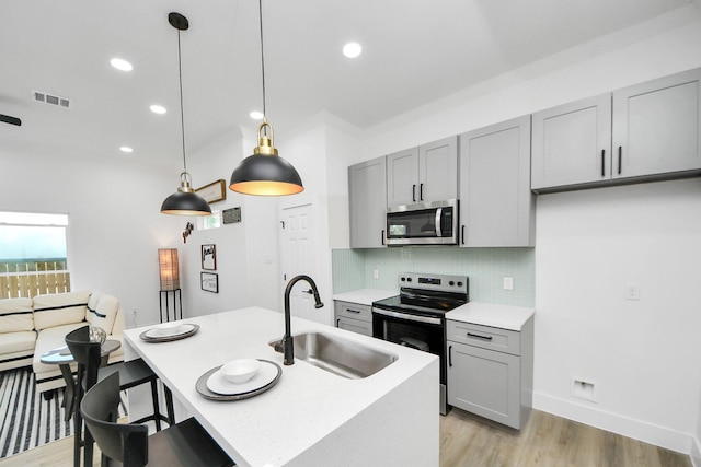 kitchen with stainless steel appliances, light wood finished floors, a sink, gray cabinetry, and visible vents