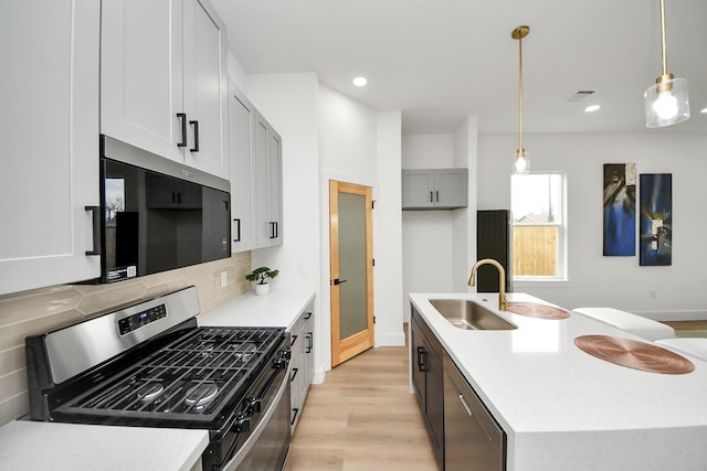 kitchen featuring decorative backsplash, light wood-style flooring, a sink, stainless steel appliances, and a kitchen island with sink