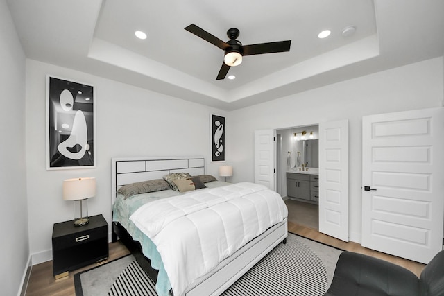 bedroom featuring connected bathroom, a raised ceiling, baseboards, recessed lighting, and wood finished floors