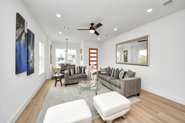 living area featuring ceiling fan with notable chandelier, visible vents, baseboards, and light wood-type flooring