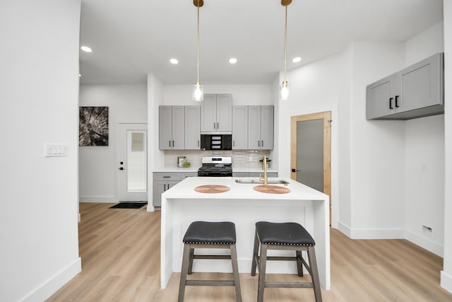 kitchen featuring stainless steel range with gas cooktop, light countertops, black microwave, baseboards, and gray cabinetry