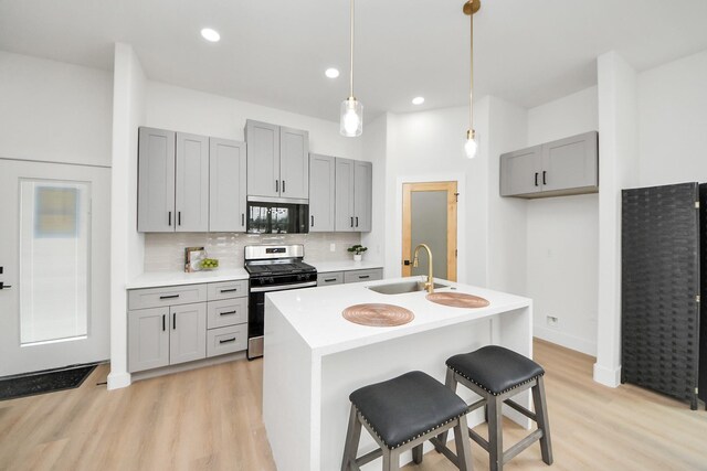 kitchen with gray cabinets, stainless steel range with gas stovetop, light wood-style floors, and a sink