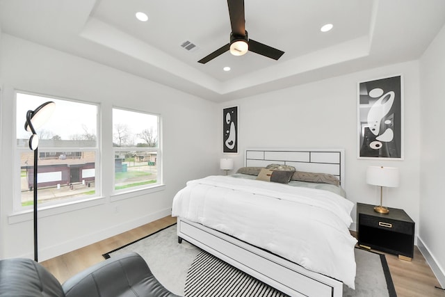 bedroom featuring light wood finished floors, a raised ceiling, visible vents, and baseboards