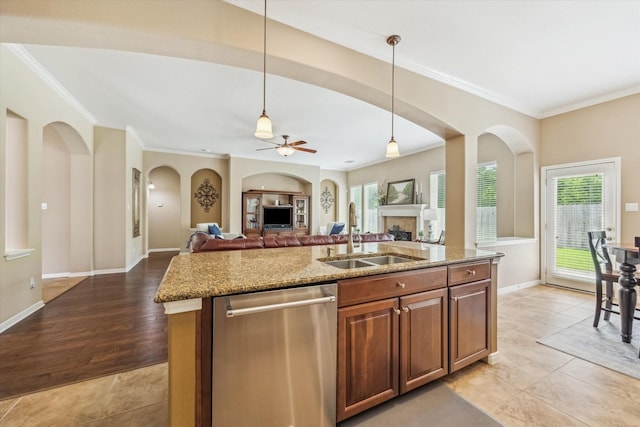 kitchen featuring arched walkways, light stone counters, dishwasher, a fireplace, and a sink