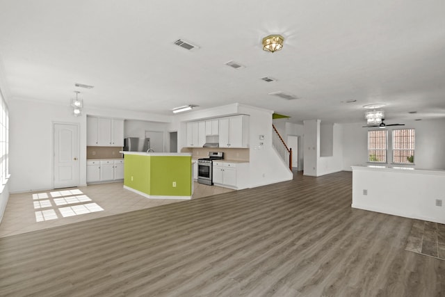 unfurnished living room featuring visible vents, baseboards, an inviting chandelier, light wood finished floors, and stairs