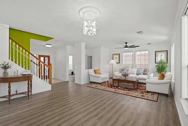 living room featuring wood finished floors, baseboards, stairs, and ceiling fan with notable chandelier