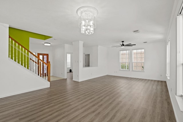 unfurnished living room featuring baseboards, stairway, wood finished floors, and ceiling fan with notable chandelier