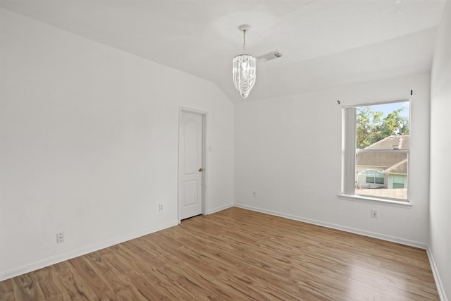 spare room with wood finished floors, a chandelier, visible vents, and baseboards