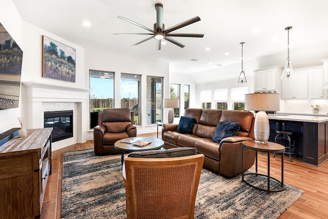 living room featuring recessed lighting, a tiled fireplace, ceiling fan, light wood-style flooring, and lofted ceiling