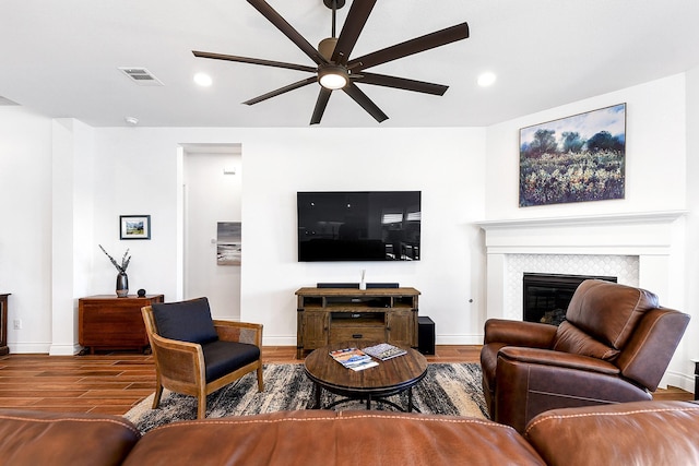 living room featuring a fireplace, a ceiling fan, visible vents, baseboards, and wood finished floors