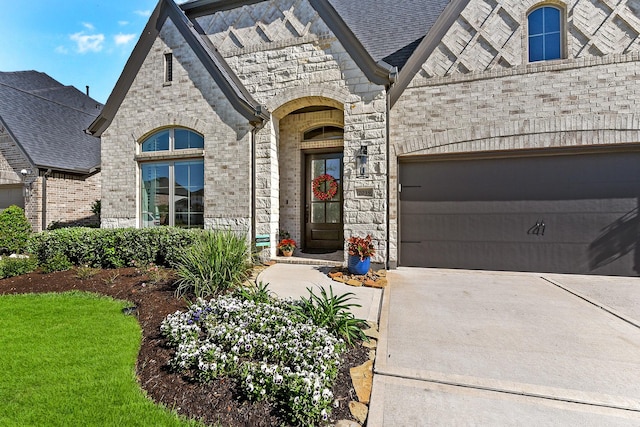 doorway to property featuring a garage, concrete driveway, brick siding, and stone siding