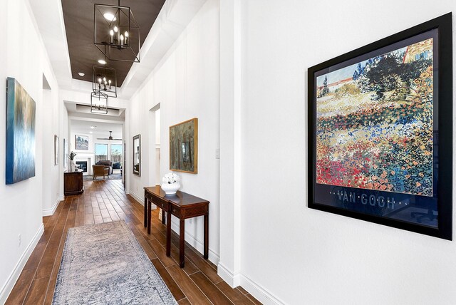 hallway featuring an inviting chandelier, dark wood-style flooring, and baseboards