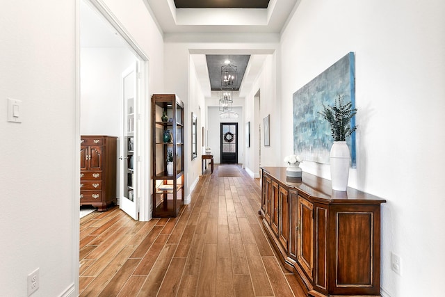hallway featuring an inviting chandelier, wood finished floors, and a tray ceiling