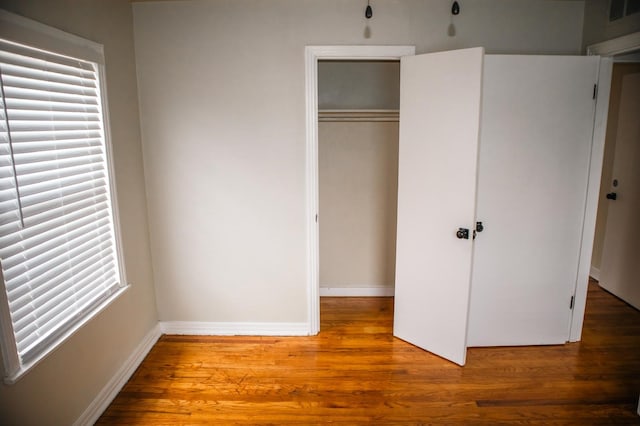 unfurnished bedroom with a closet, visible vents, wood finished floors, and baseboards