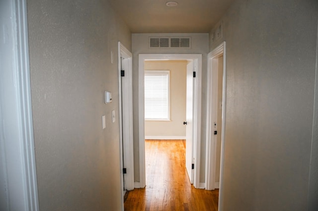corridor featuring visible vents, wood finished floors, and baseboards