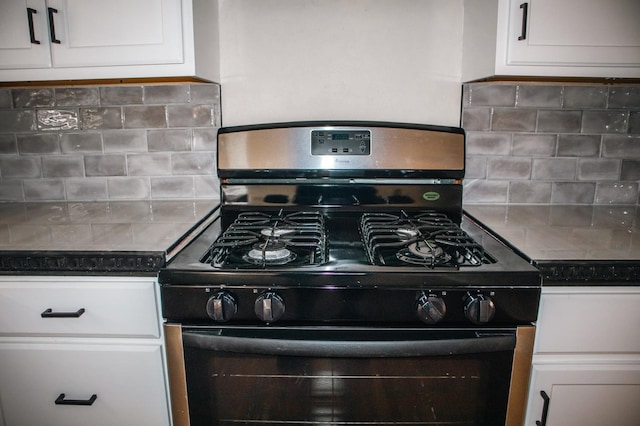 kitchen with dark countertops, white cabinets, gas range, and decorative backsplash