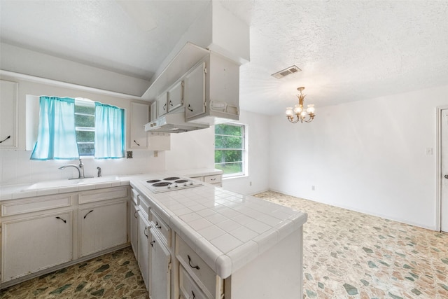 kitchen with tile counters, visible vents, under cabinet range hood, white electric cooktop, and a notable chandelier