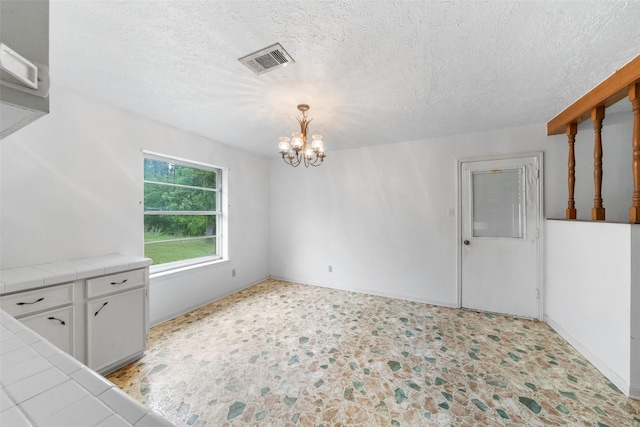unfurnished dining area featuring a chandelier, visible vents, a textured ceiling, and baseboards
