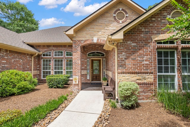 doorway to property featuring a shingled roof and brick siding