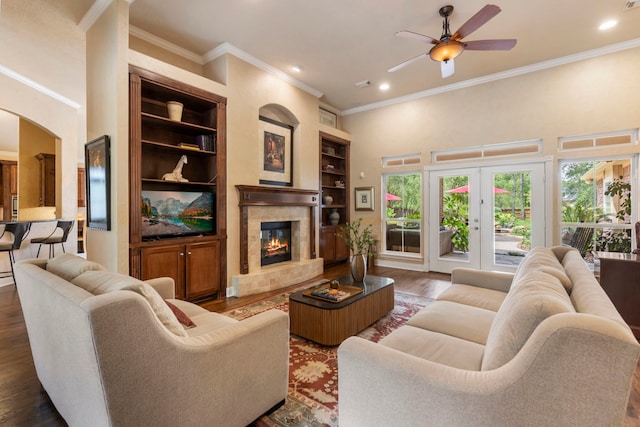 living room with a ceiling fan, dark wood-style flooring, crown molding, built in features, and a glass covered fireplace
