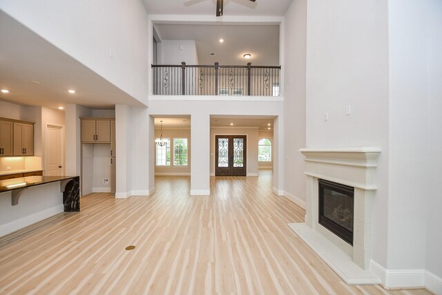 6939 Shoreline View Dr, Katy, TX 77493 - unfurnished living room with a high ceiling, a glass covered fireplace, ceiling fan with notable chandelier, and light wood-type flooring