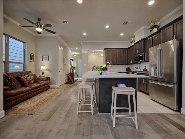 kitchen with crown molding, dark brown cabinetry, stainless steel appliances, and open floor plan