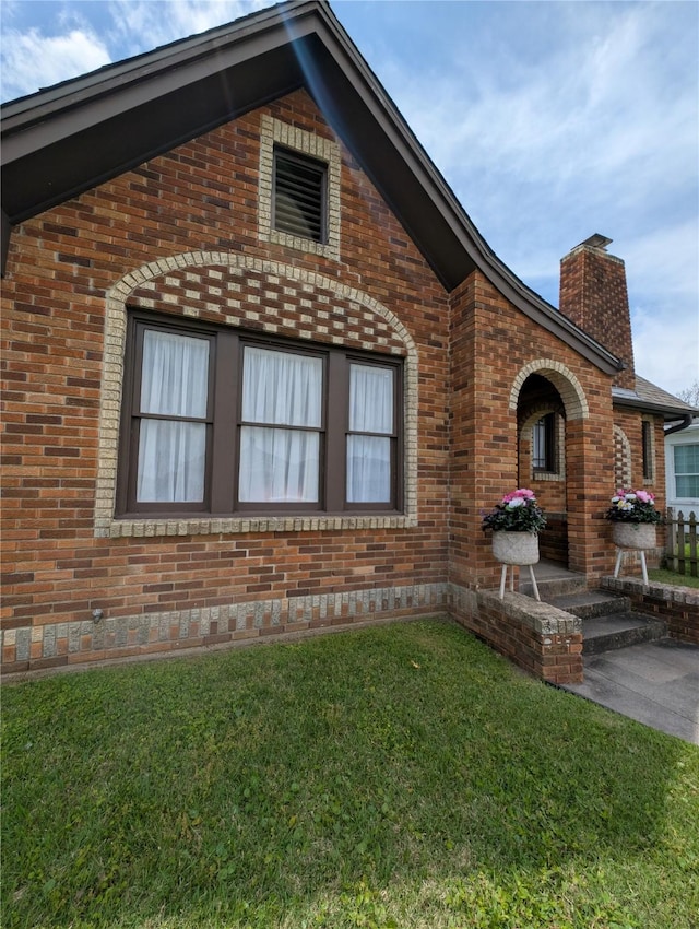exterior space with a lawn, a chimney, and brick siding