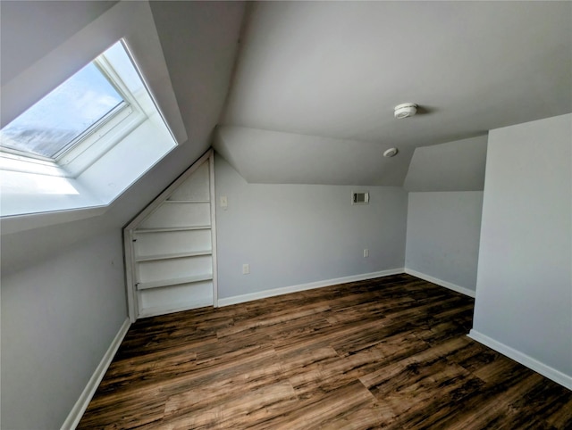 additional living space featuring baseboards, lofted ceiling with skylight, and dark wood-style floors