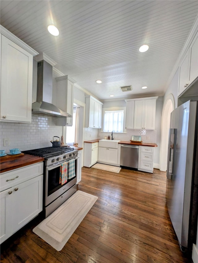 kitchen featuring wall chimney range hood, tasteful backsplash, stainless steel appliances, and white cabinets