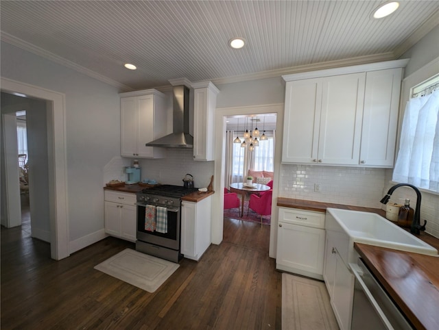 kitchen featuring wall chimney range hood, stainless steel appliances, wooden counters, and plenty of natural light