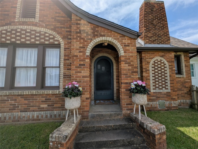doorway to property with brick siding, a shingled roof, and a chimney
