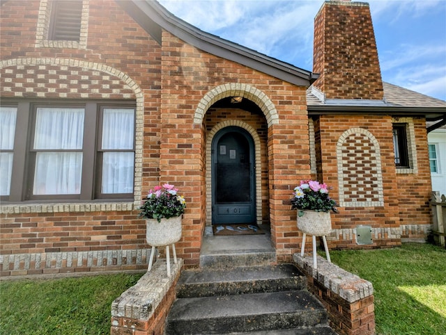 entrance to property with roof with shingles, a chimney, and brick siding