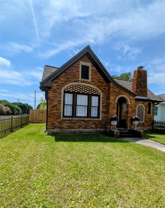 view of front of home featuring a chimney, brick siding, fence, a front lawn, and a shingled roof
