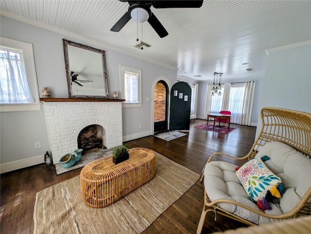 living area featuring ceiling fan, crown molding, arched walkways, a brick fireplace, and baseboards