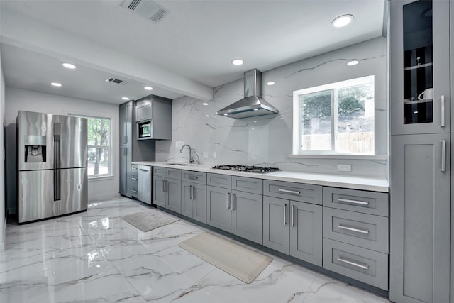 kitchen with a sink, gray cabinets, stainless steel appliances, and wall chimney range hood