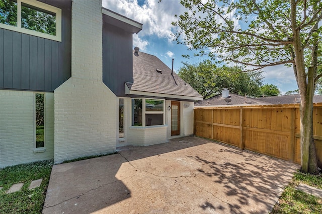 rear view of property featuring fence, a patio area, roof with shingles, and brick siding