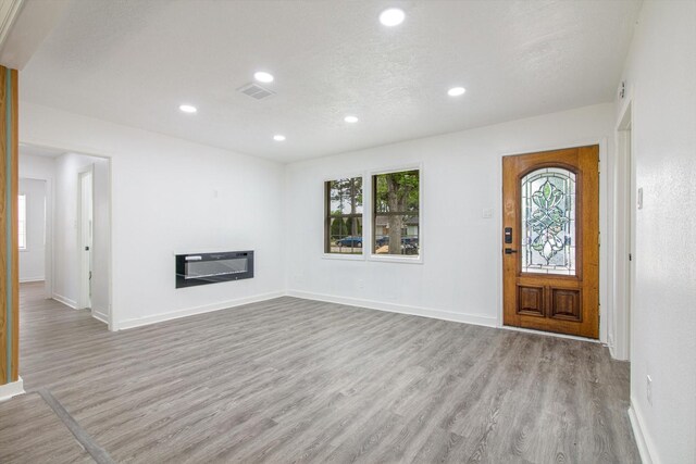 foyer featuring recessed lighting, wood finished floors, heating unit, a glass covered fireplace, and baseboards