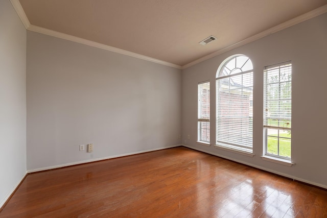 empty room featuring plenty of natural light, ornamental molding, and wood finished floors